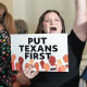 Senfronia Thompson, left, walks past a crowd of people into the House Chamber, a person holds a sign that says "put Texans first"