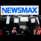 News anchors work at Newsmax's booth.