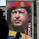 People walk past a mural of Hugo Chavez on the side of a building outside