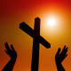 Silhouetted hands raised towards a bright sun and a wooden cross.