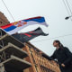A demonstrator waves the Serbian flag in in Belgrade, Serbia, in front of a run-down building.