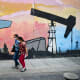 Women walk past a mural depicting an oil pump on April 14, 2021 in a street of Caracas, Venezuela.