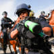 A police officer holds a weapon to the camera as protesters face off with police outside of a federal building in downtown Los Angeles for an anti-Trump "No Kings Day" demonstration.