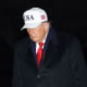 Donald Trump walks at the White House at night, wearing a white USA hat.