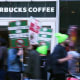 People blurred in motion hold signs in front of a Starbucks Coffee location.