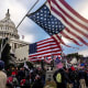 People, many with American flags, surround the Capitol.