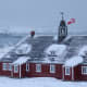 Greenland flag flies over building with Danish Navy ship in background