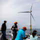 People look at a wind turbine in the water.