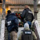 Four people with "police" and "ICE" on their uniforms knock on the door to a home decorated with a holiday wreath and string lights.