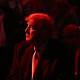 Donald Trump looks into the distance. He and the crowd are basked in red light.