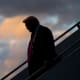Donald Trump, silhouetted, descends an outdoor staircase. A sky full of colorful clouds is behind him.