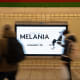 People, blurred in motion, walk past an advertisement for the movie "Melania."