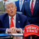 President Donald Trump, center, surrounded by members of the House and Senate in the Oval Office. Out of focus on the desk is a red hat that says "AMERICA IS BACK!"