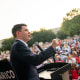 James Talarico speaks at a podium. A crowd of people sits in front of him in a lawn.
