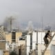 There is a man climbing up stairs while there is smoke rising inthe skyline of Tehran in the background.
