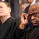 Clarence Thomas adjusts his glasses as Samuel Alito leans back in the background.