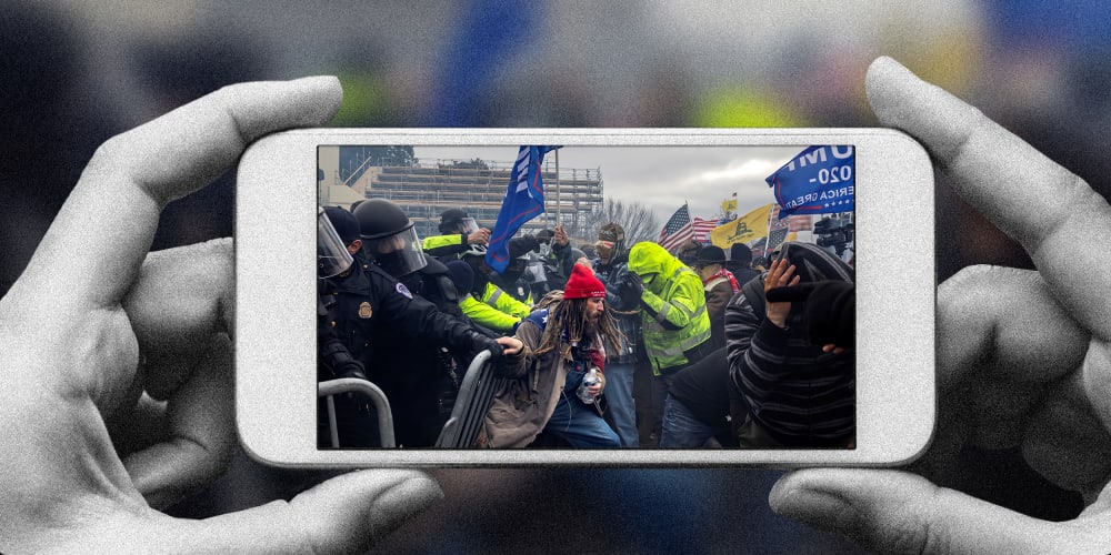 Photo illustration of a hands holding a phone with the image of Trump supporters clashing with the police and security forces as people try to storm the US Capitol.