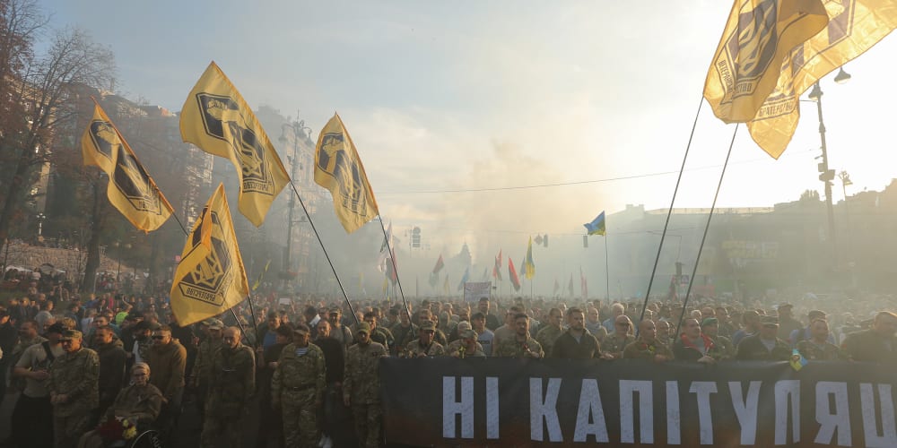 Image: People in the uniform carrying Azov battalion flags and a banner saying "No Capitulation" through the smoke during a rally in Kyiv, Ukraine, Oct. 14, 2019.