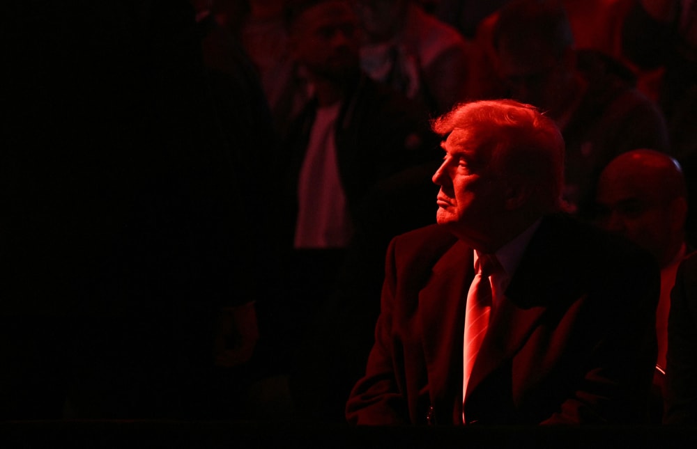 Donald Trump looks into the distance. He and the crowd are basked in red light.