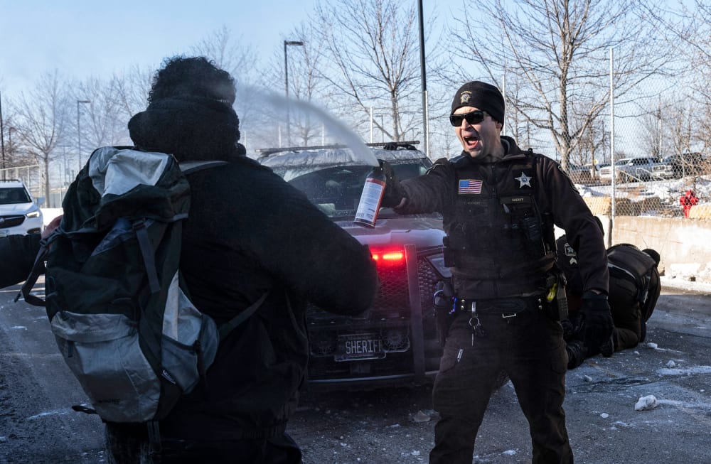 An officer sprays a protester with irritant gas in front of a police car.