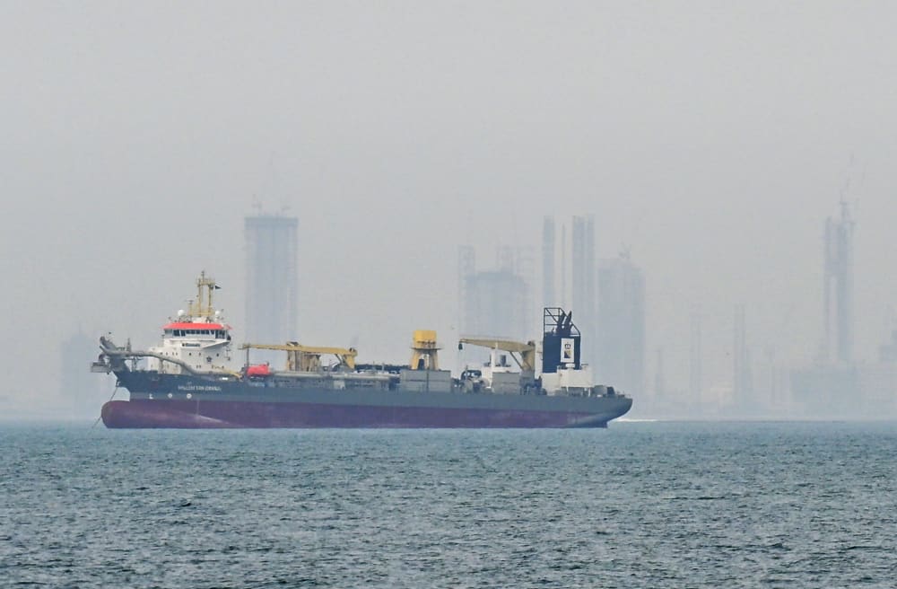 A ship is seen in the foreground and the skyline is seen in the background in fog.