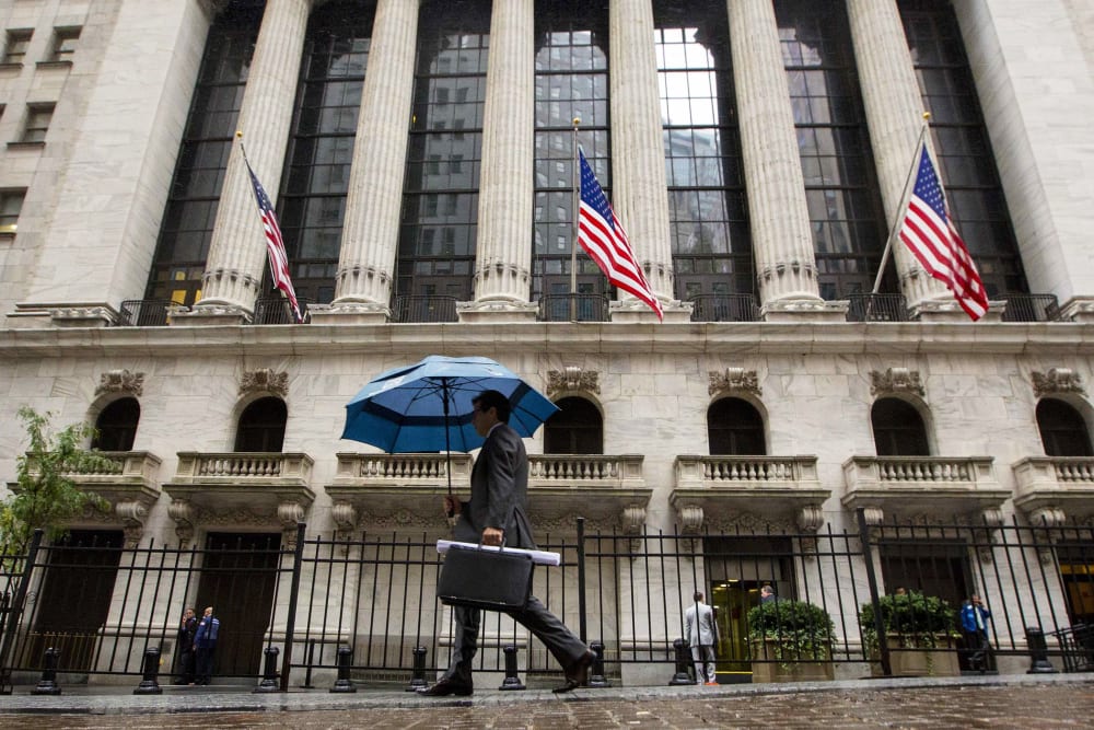 A man carries an umbrella in the rain as he passes the New York Stock Exchange on Oct. 16, 2014.