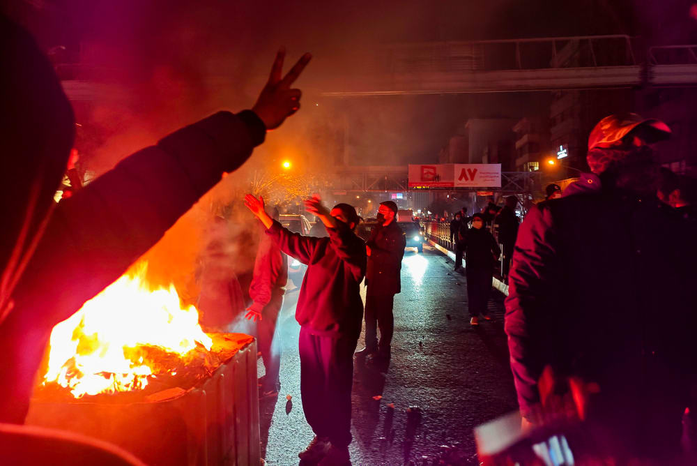 People gather around a fire lit on the streets of Tehran.