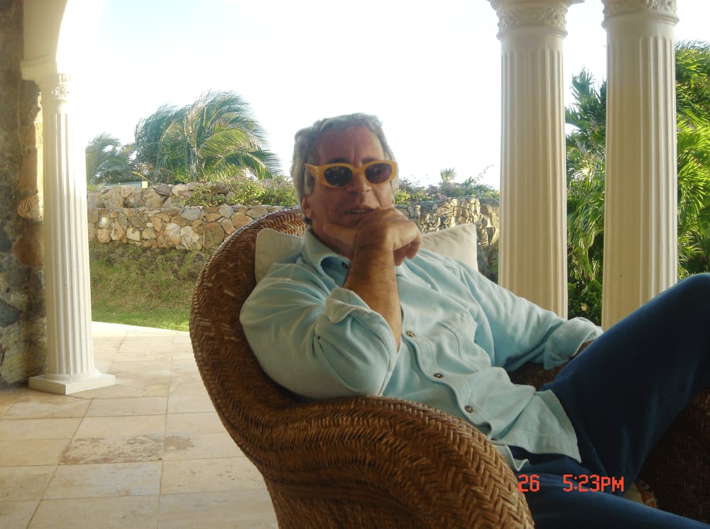 Jeffrey Epstein sits at a patio wearing yellow framed sunglasses.