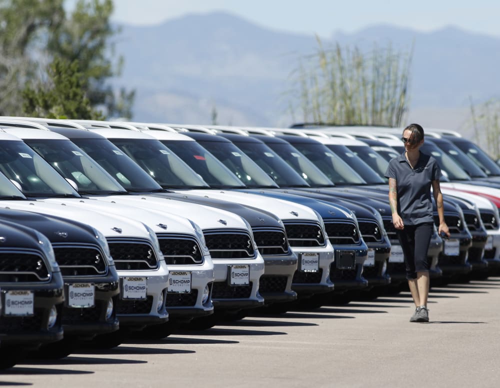 A lot technician passes by a long line of unsold cars at a dealership in Highlands Ranch