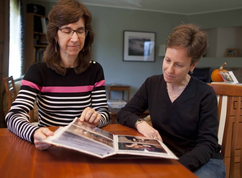In this photo taken Nov. 12, 2012, Karen Golinski (left) and Amy Cunninghis look over a photo album of their wedding photos in San Francisco. Golinski wanted to enroll her spouse in her employer-sponsored health plan. Four years later, her request...