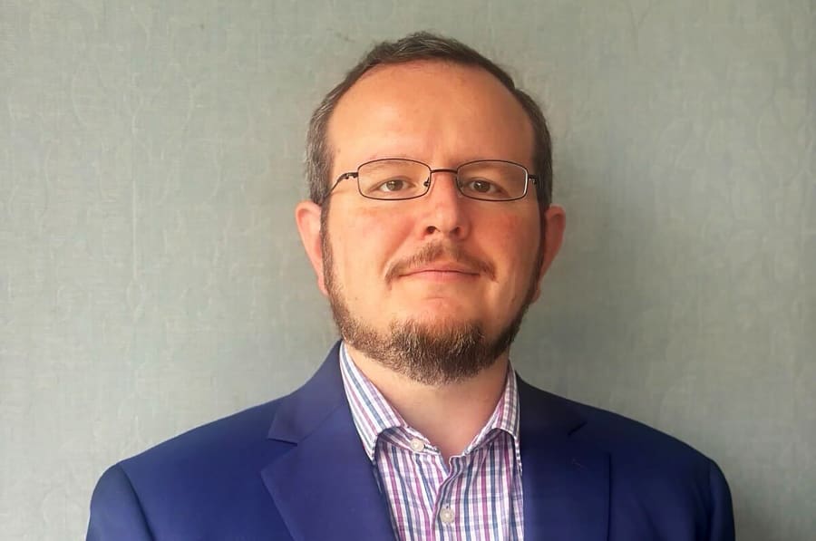 Ryan Schwank stands in front a wall as he looks at the camera.