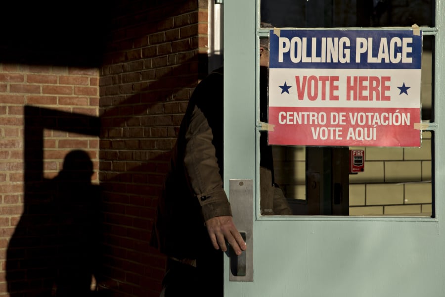 A person slips into a building with a light blue door. A sign on the door says "Polling Place Vote Here Centro De Votación Vote Aqui."