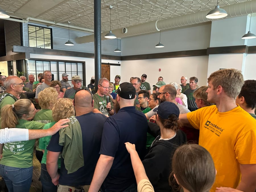 A group of people huddling around Clint Twedt-Ball reach their arms out toward him.