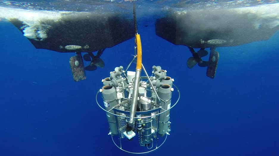 A sophisticated water column monitoring instrument suspended beneath a vessel, equipped with multiple sampling bottles and sensors. The system is used to collect water quality data, including temperature, dissolved oxygen, and contaminants in subsea oil spill response efforts.