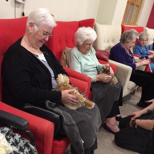 4 Care Home Residents handling chickens while sat in arm chairs