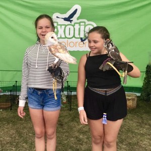 2 girls at Nearly Festival holding an owl each, with the Exotic Explorers logo in the background