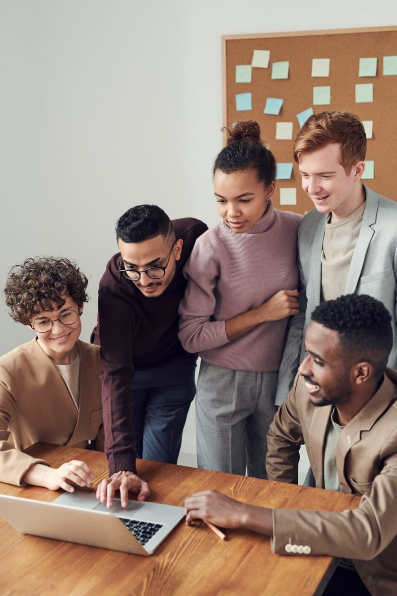 A diverse group of employees standing over a laptop