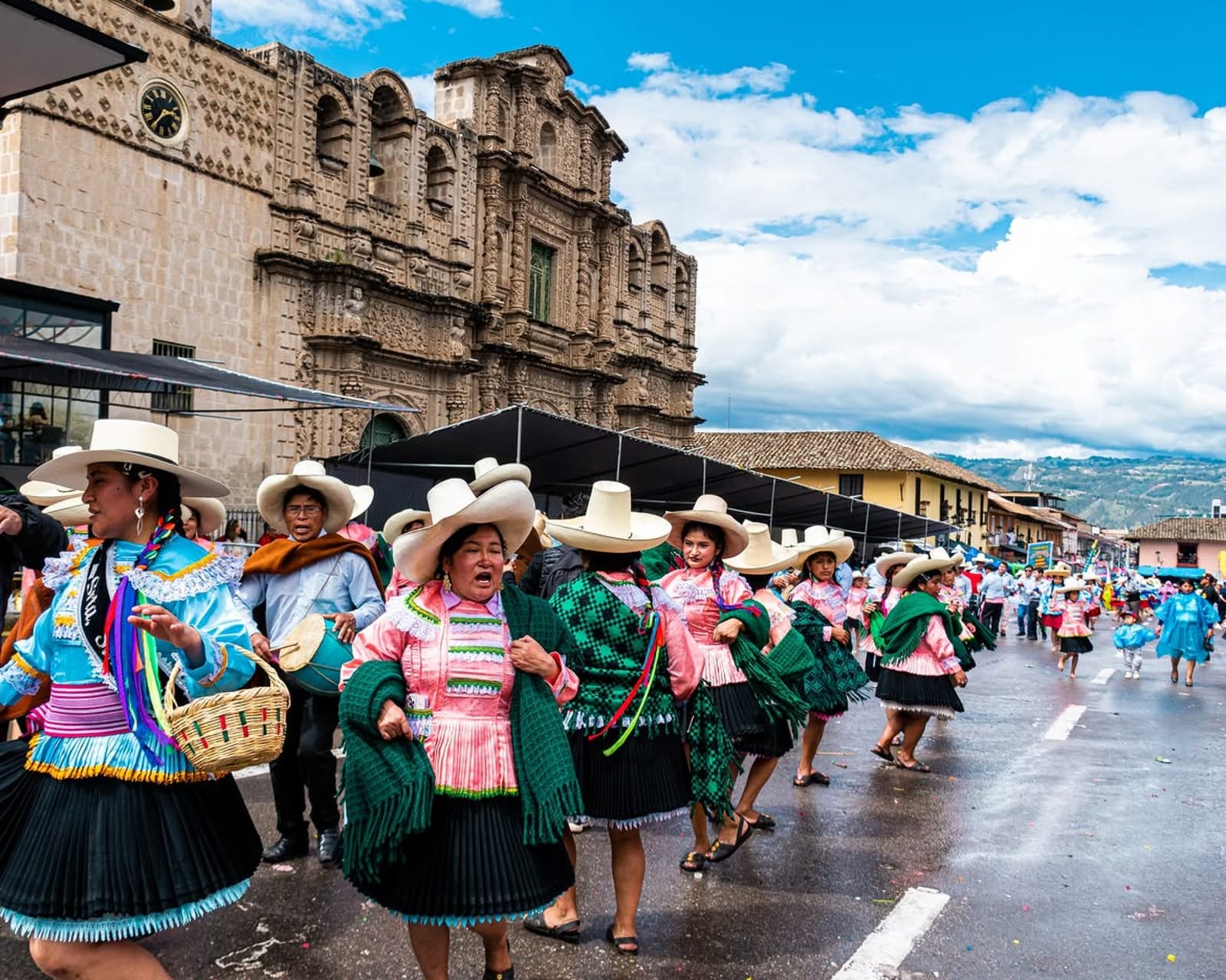 Danzantes del carnaval con sombrero de paja, pollera y manta verde pasan frente a la Catedral de Cajamarca