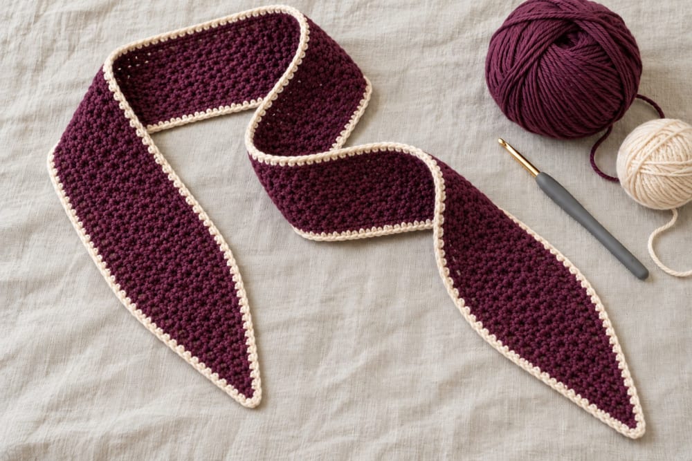 Écharpe Vercors au crochet, au point tissé, en mérinos prune avec une bordure crème, une pelote et un crochet ergonomique