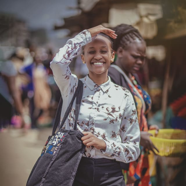 A smiling woman in a patterned blouse at an outdoor market