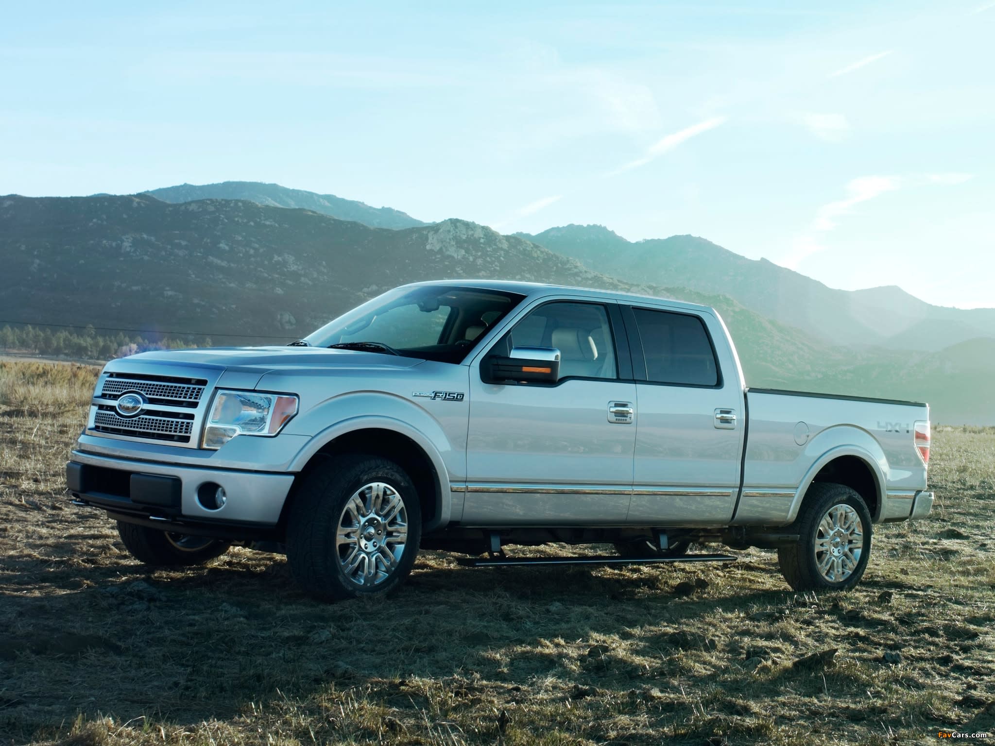 White 2008 Ford F-150 with front and rear seats parked in a dirt field with some grass growing around it and hills in teh background.