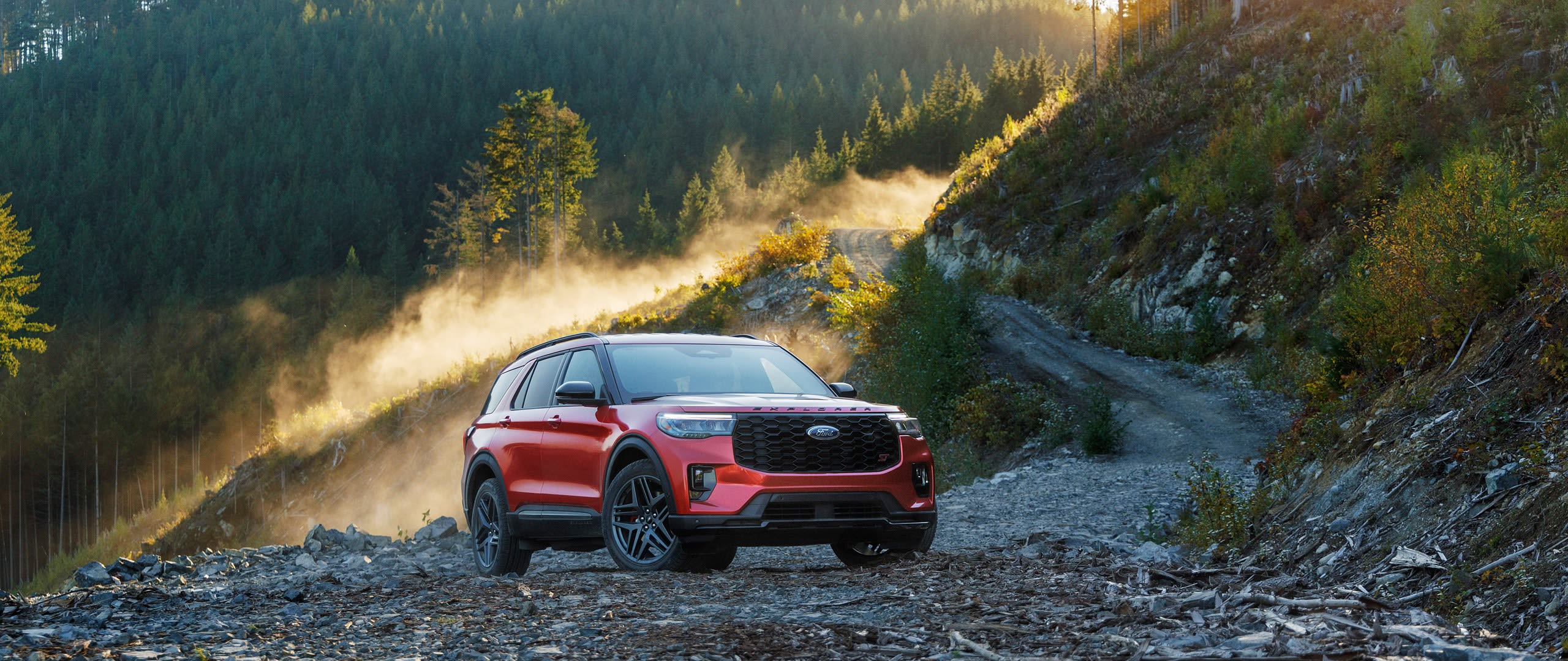 Reliable red Ford Explorer parked in a trail in the mountains, with estimated fuel economy of 21 mpg in the city and 28 mpg on the highway.