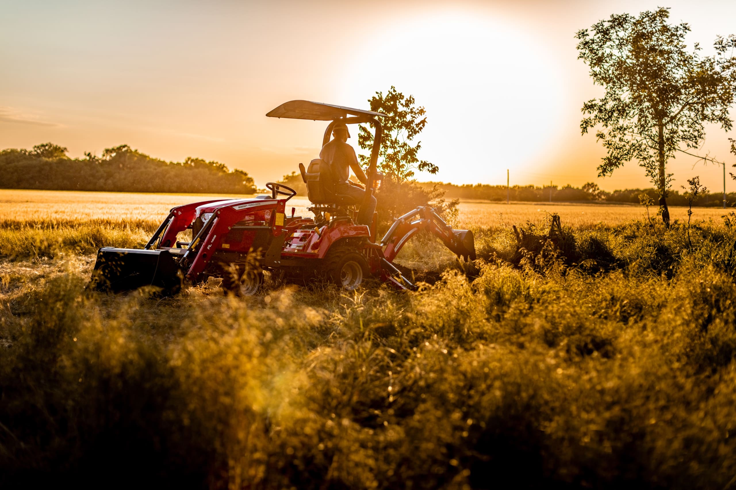 MF GC1700 sub-compact tractor with backhoe in a field at sunset.