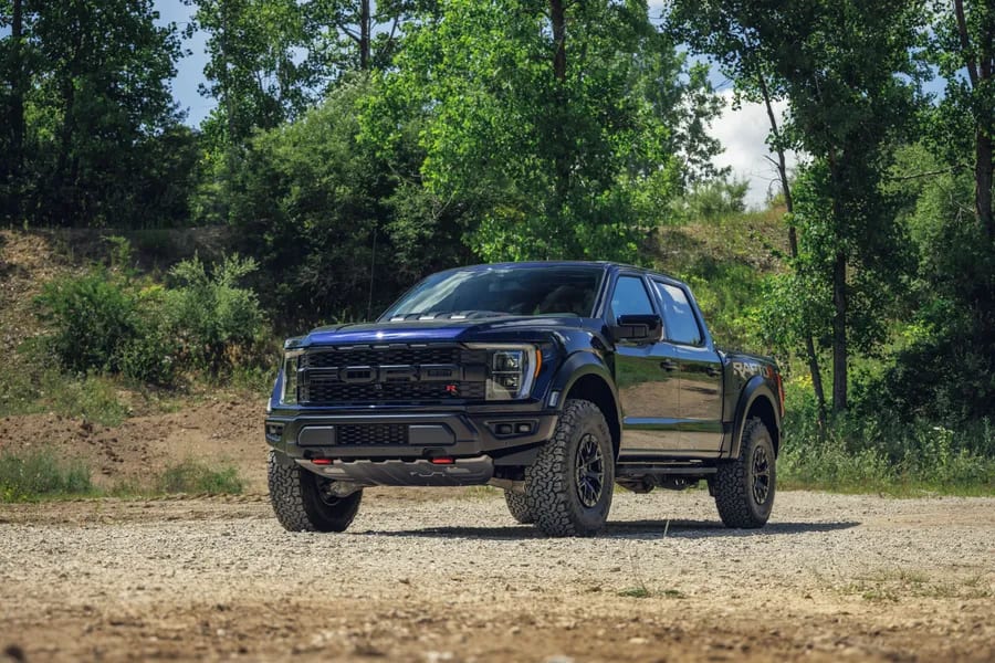 Black Ford F150 diesel vehicle parked in front of trees on a gravel road.