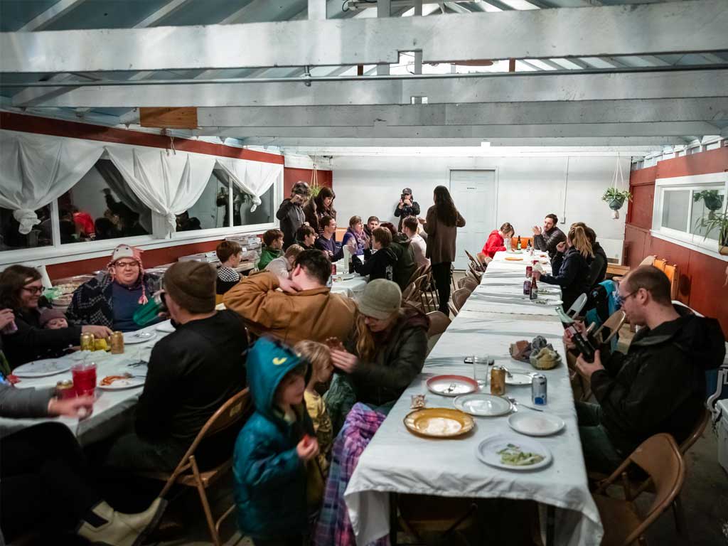 Group of people enjoying a pizza party in a cozy lodge setting, sharing food and laughter, with some capturing moments on cameras, reflecting the camaraderie of Murmur Creative's retreat activities.