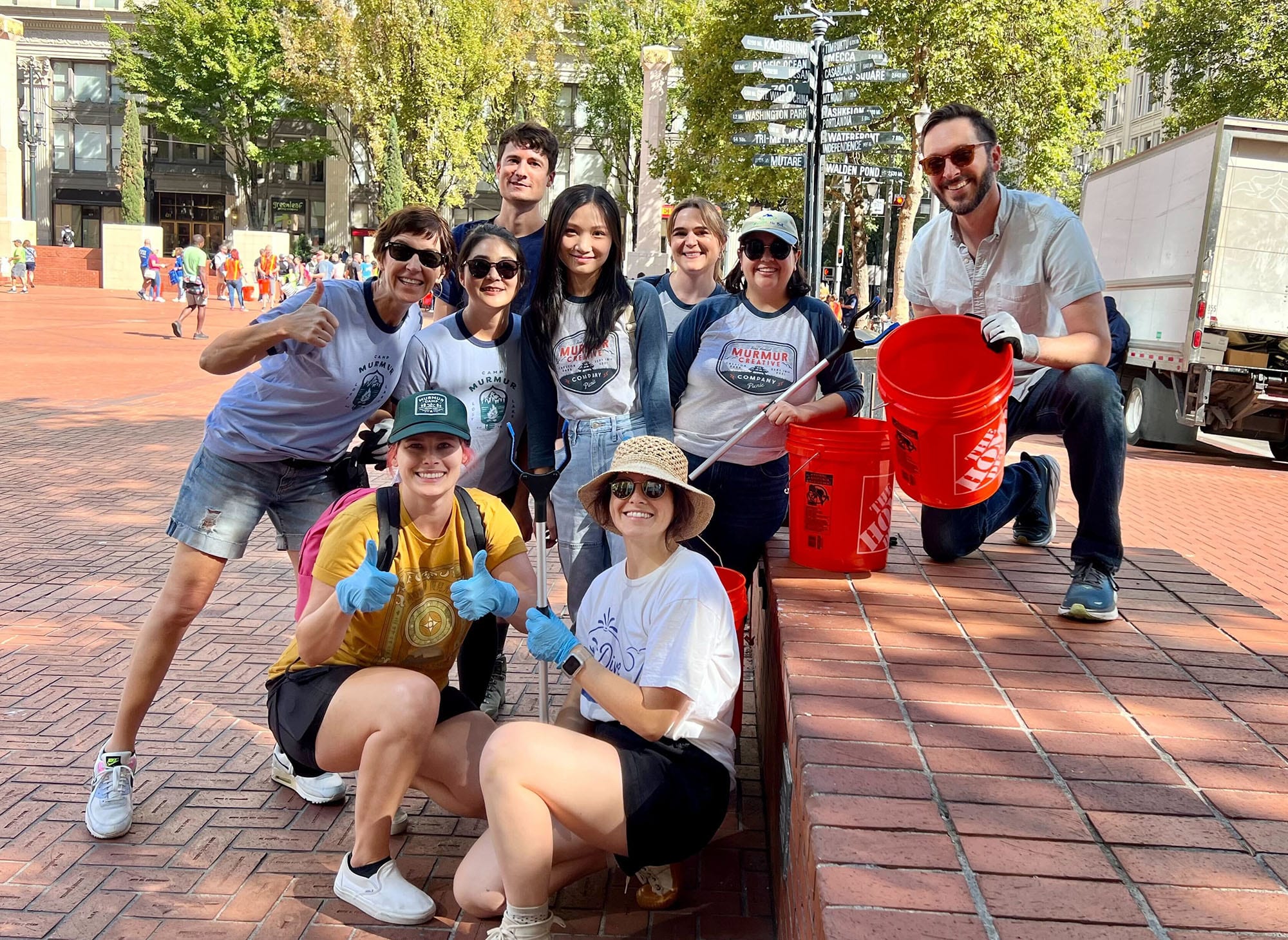 Group of volunteers from Murmur Creative engaging in community service, smiling and posing with gardening tools and red buckets in a downtown Portland setting.