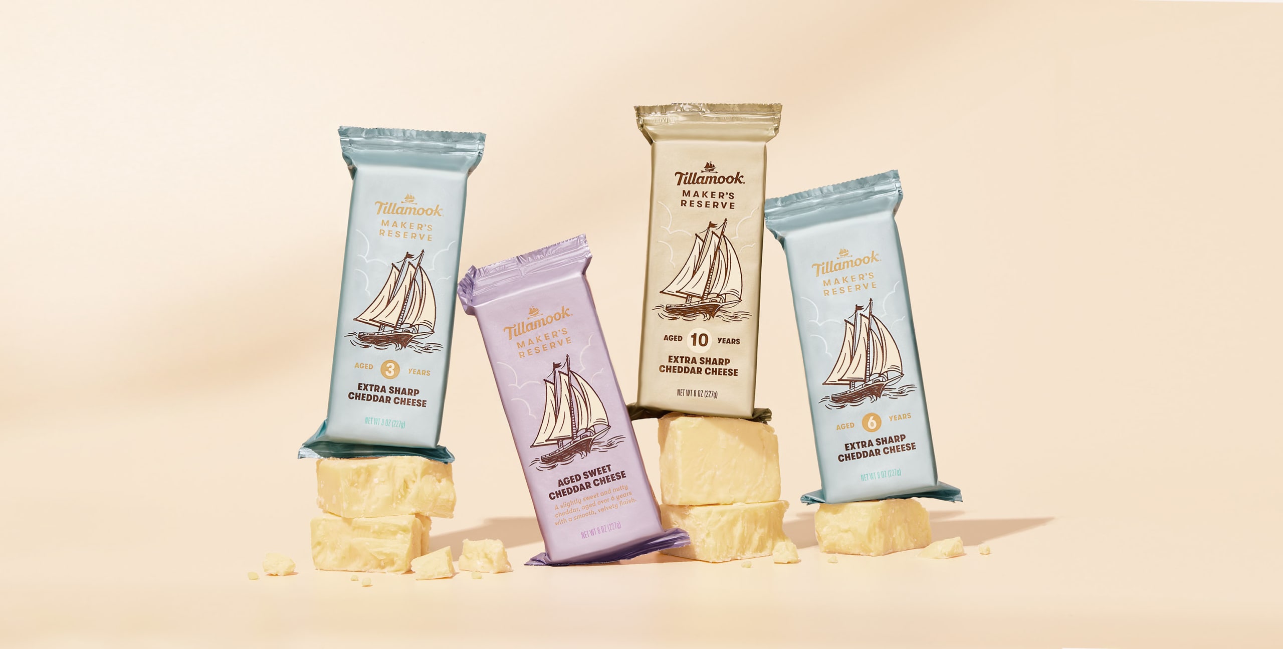 Tillamook Maker's Reserve cheese packaging featuring four distinct bars, each labeled with aging details and a sailboat illustration, arranged artistically on a light pastel background.