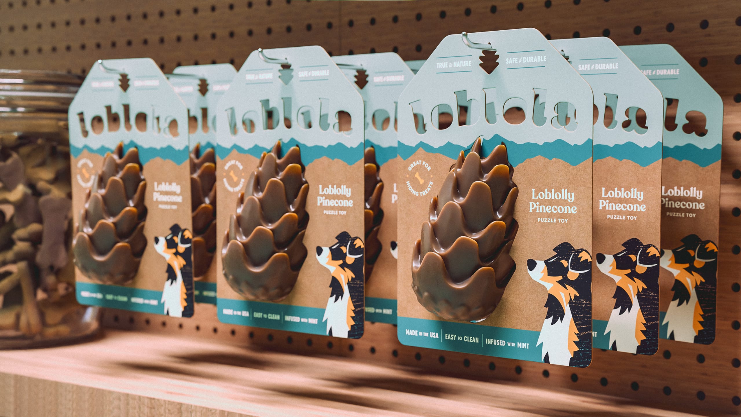 Loblolly Pinecone puzzle toy packaging displayed on a wooden shelf, featuring a playful dog illustration and eco-friendly branding, highlighting its features like "safe & durable" and "made in the USA."