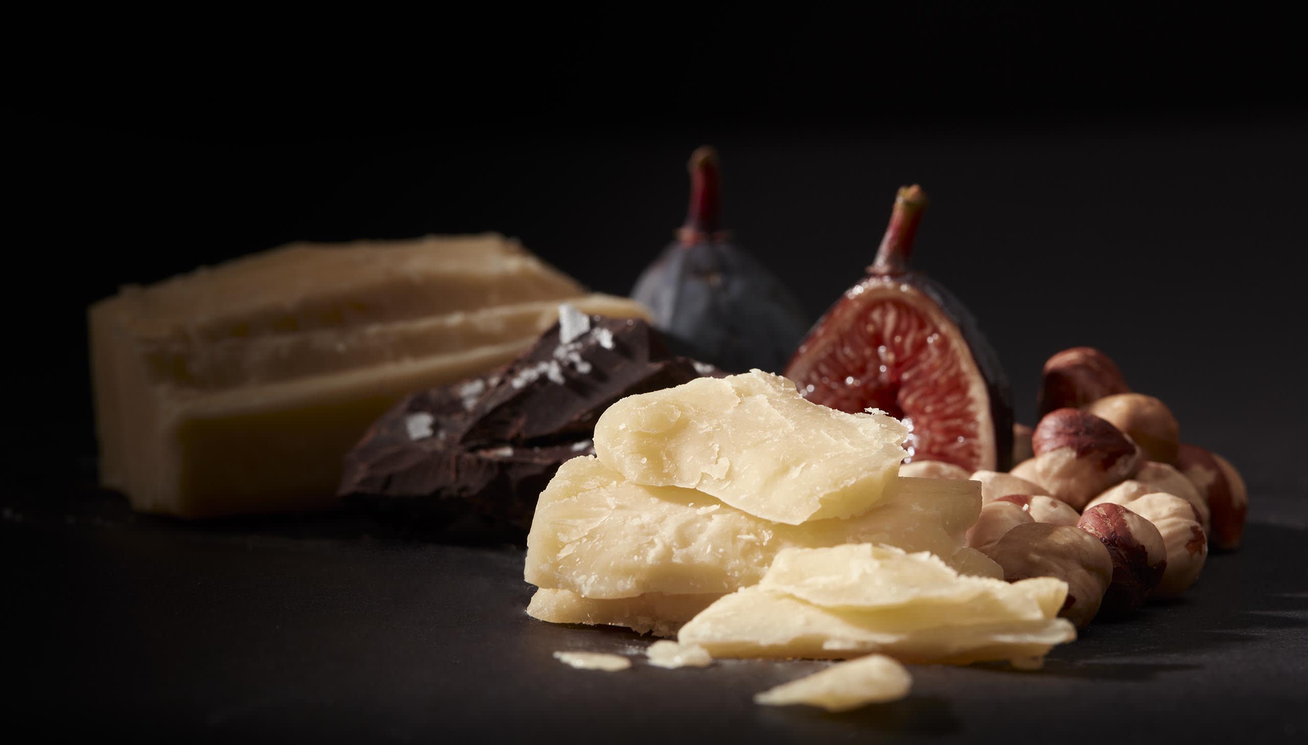 Aged cheddar cheese slices with dark chocolate, fresh figs, and hazelnuts on a dark background, showcasing artisanal cheese pairings for Tillamook Maker's Reserve.