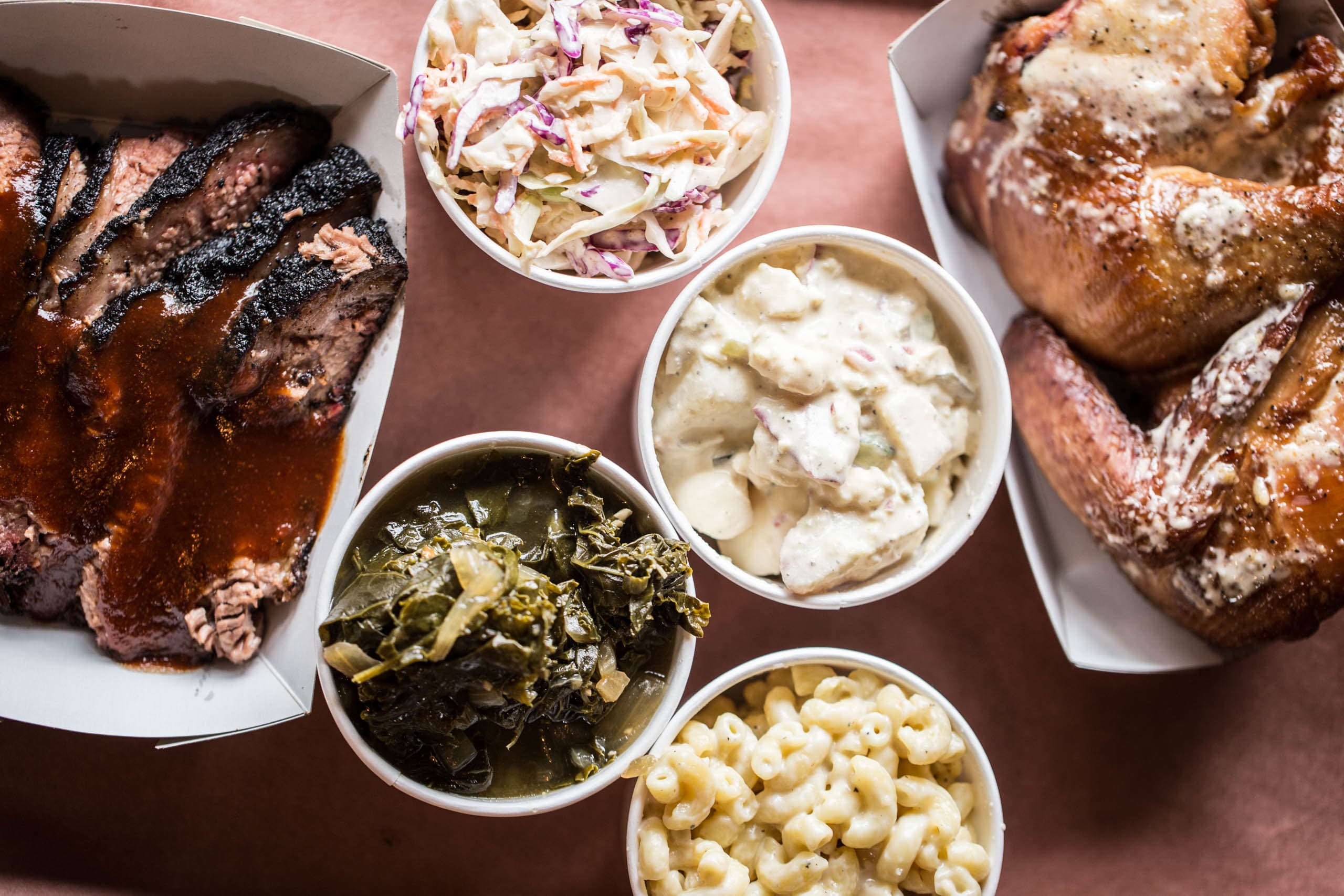 Barbecue platter featuring sliced brisket with sauce, coleslaw, potato salad, collard greens, and macaroni and cheese, representing Russell St. BBQ's offerings in Portland, Oregon.